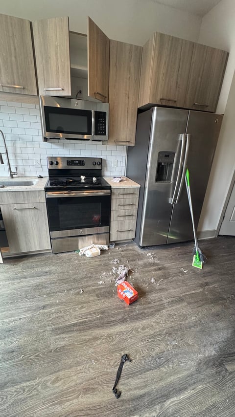 Modern kitchen under renovation with light wood cabinets, stainless steel appliances, white subway tile backsplash, and construction debris on dark wood floor