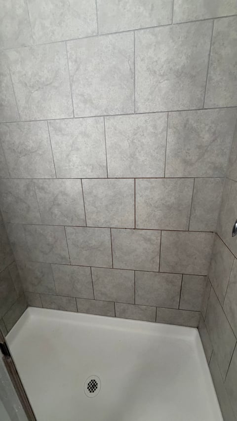 Shower stall with light gray ceramic tile walls in rectangular pattern and white base pan