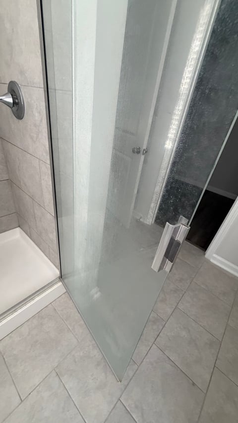 Modern glass shower enclosure with frosted panels in a bathroom with gray tile flooring