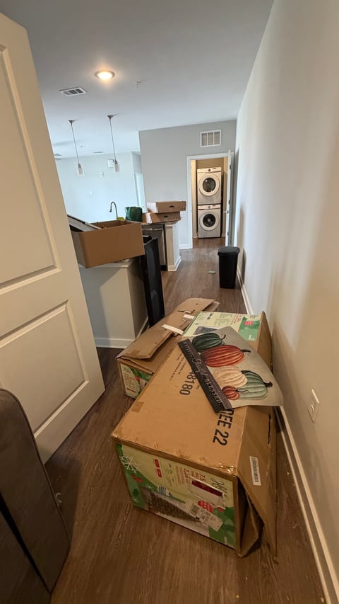 Moving boxes stacked in a narrow hallway of a home with kitchen and laundry room visible in background
