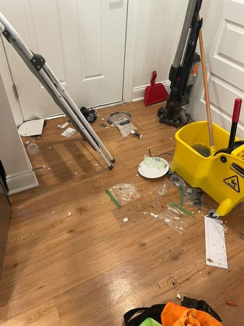 Home renovation workspace with ladders, painting equipment, and protective coverings scattered across wooden floor