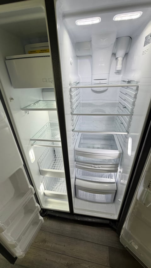 Open empty refrigerator with both doors ajar showing clear shelves and drawers inside
