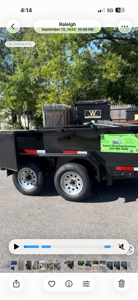 Black dual-axle dump trailer with red and white reflective striping and Leons Cleaning Services contact information displayed on the side
